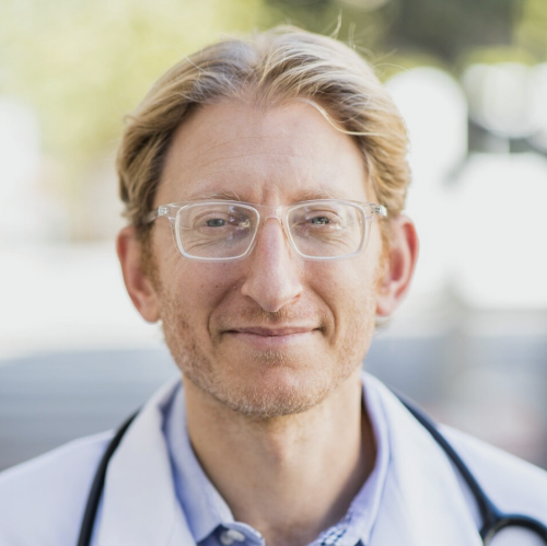 Photo of Scott Sherr, a white man in a doctors coat with a stethoscope, smiling at the camera.